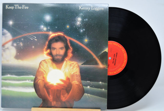 Vinyl record with cover featuring a person holding a light bulb against a cosmic background, titled 'Keep The Fire' by Kenny Loggins.