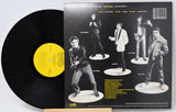 Vinyl record titeled Kihnspiracy with a yellow label and album cover featuring band members on white stands.