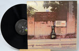 Vinyl record with cover featuring a brick wall and bottle, resembling the Abbey Road album cover.