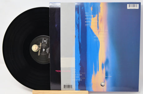 A vinyl record partially pulled from its sleeve, photographed on a white background. The record is black with a visible Optimum Records label, and the sleeve features an abstract blue, gray, and orange design.