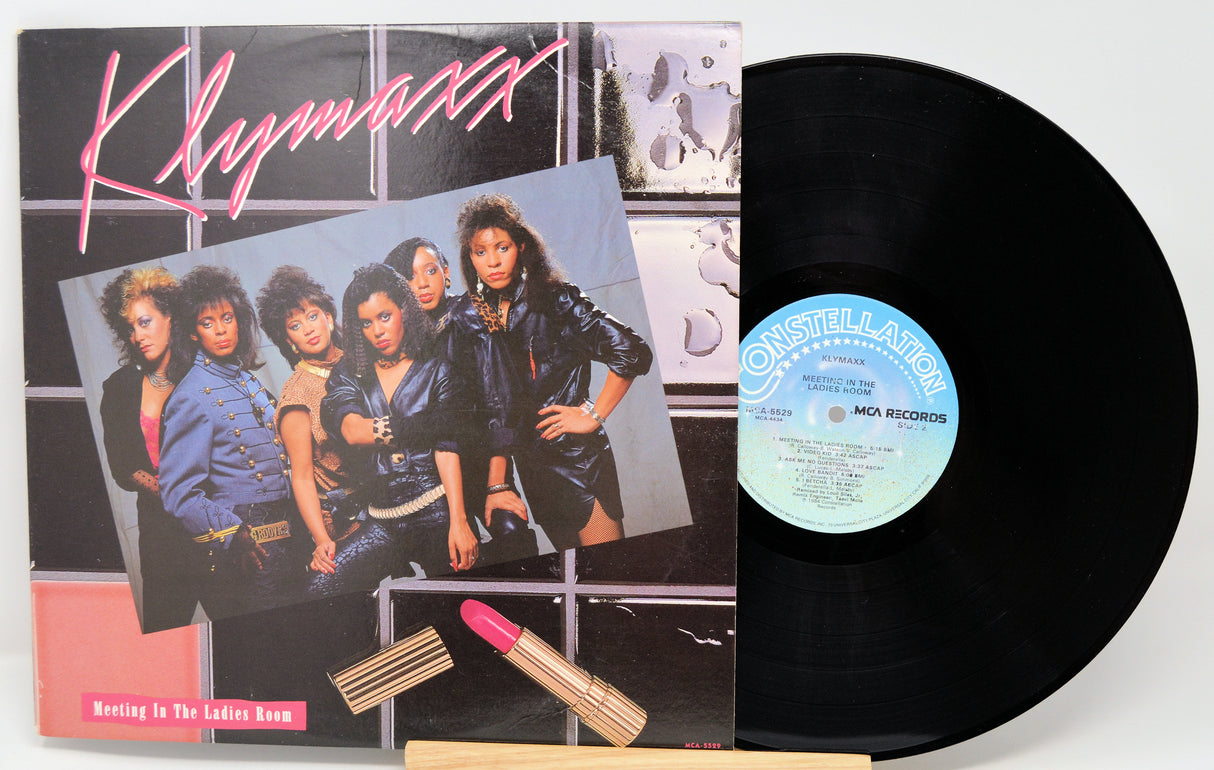 Vinyl record with a colorful cover featuring a group of women and a lipstick on a white background.