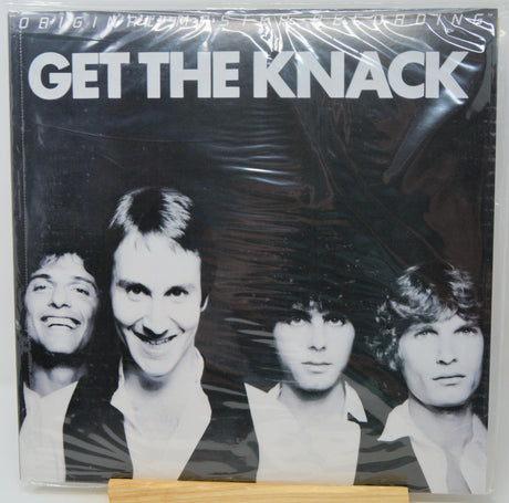 A vinyl record sleeve for the band 'Get The Knack' wrapped in clear plastic, displayed on a small wooden stand against a white background.