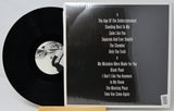 Vinyl record with cover displaying album tracklist on a light gray background