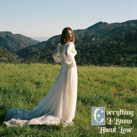 Woman in a white dress standing in a grassy field with mountains in the background