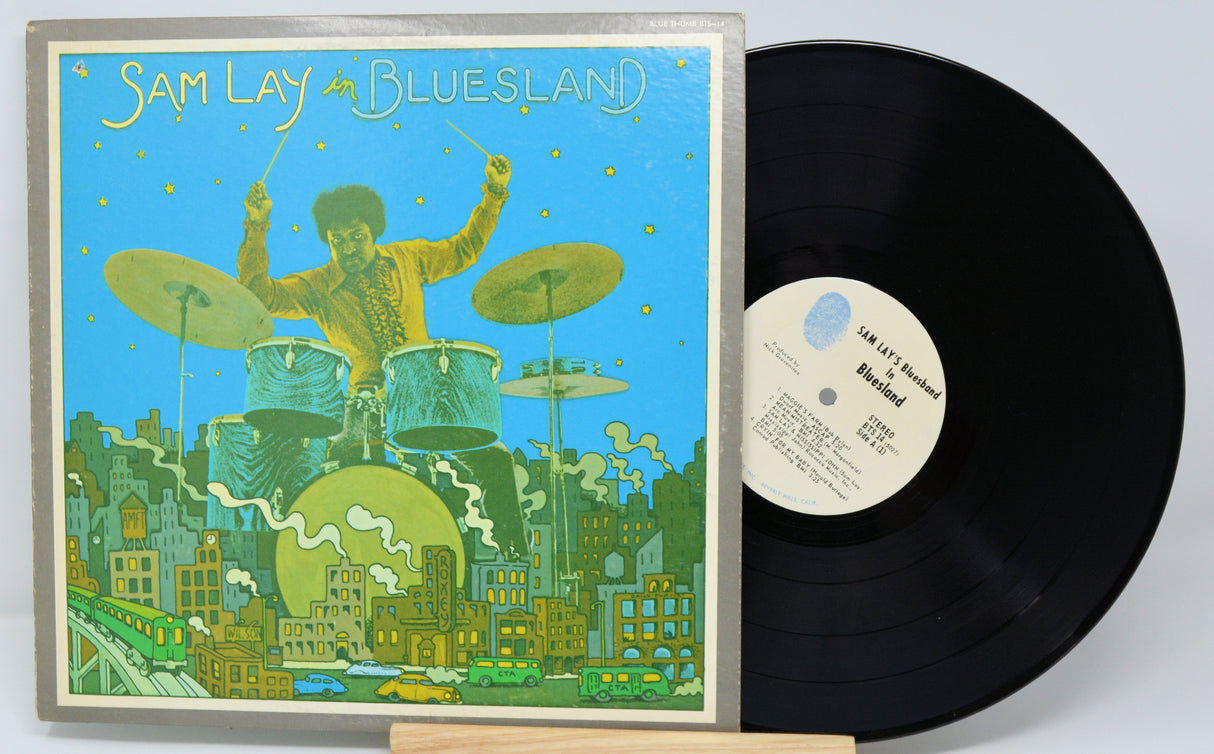 Vinyl record with a colorful cover featuring a drummer and cityscape, on a light gray background.