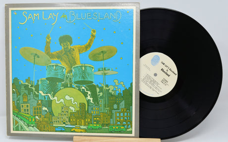 Vinyl record with a colorful cover featuring a drummer and cityscape, on a light gray background.