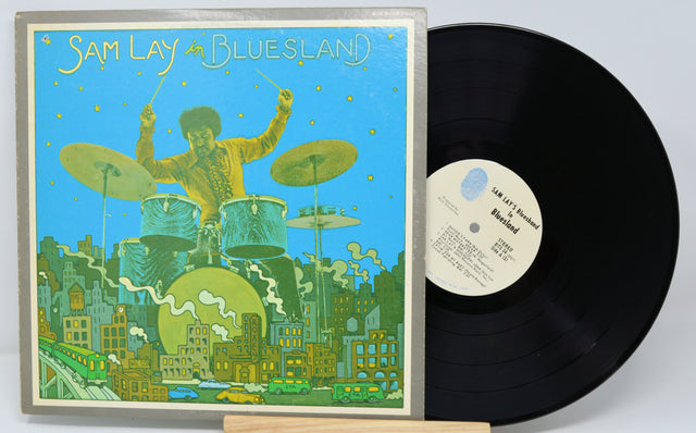 Vinyl record with a colorful cover featuring a drummer and cityscape, on a light gray background.