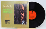 Vinyl record with cover featuring a portrait and text, on a light gray background