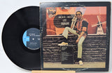 Vinyl record with cover featuring a musician on a bench, on a white background