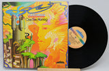 A vinyl record and its illustrated album cover for Lighthouse's 'One Fine Morning' displayed on a small wooden stand against a light gray background.