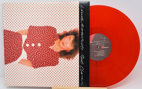 Vinyl record album with a red-and-white polka dot cover showing a woman in a red polka dot dress, partially pulled from a translucent bright red vinyl record on a stand.
