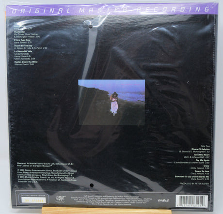 Back cover of a vinyl record package in plastic shrink-wrap, showing the track listing, barcode, and a small central album art photo of a person standing on a cliff by the sea.
