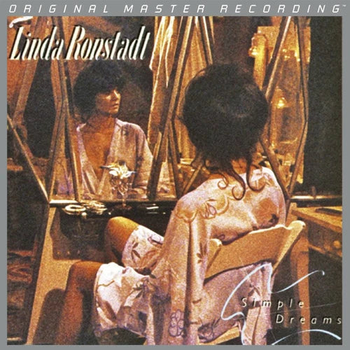 Album cover for Linda Ronstadt's 'Simple Dreams' featuring a warm-toned photograph of a woman seated in front of mirrors, wearing a light patterned robe. The title and artist name are printed at the top.