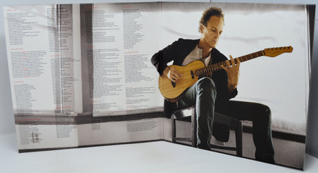 A large printed panel or poster featuring a seated man playing an acoustic guitar, with dense text columns visible on the left side. The panel is photographed against a plain light background.