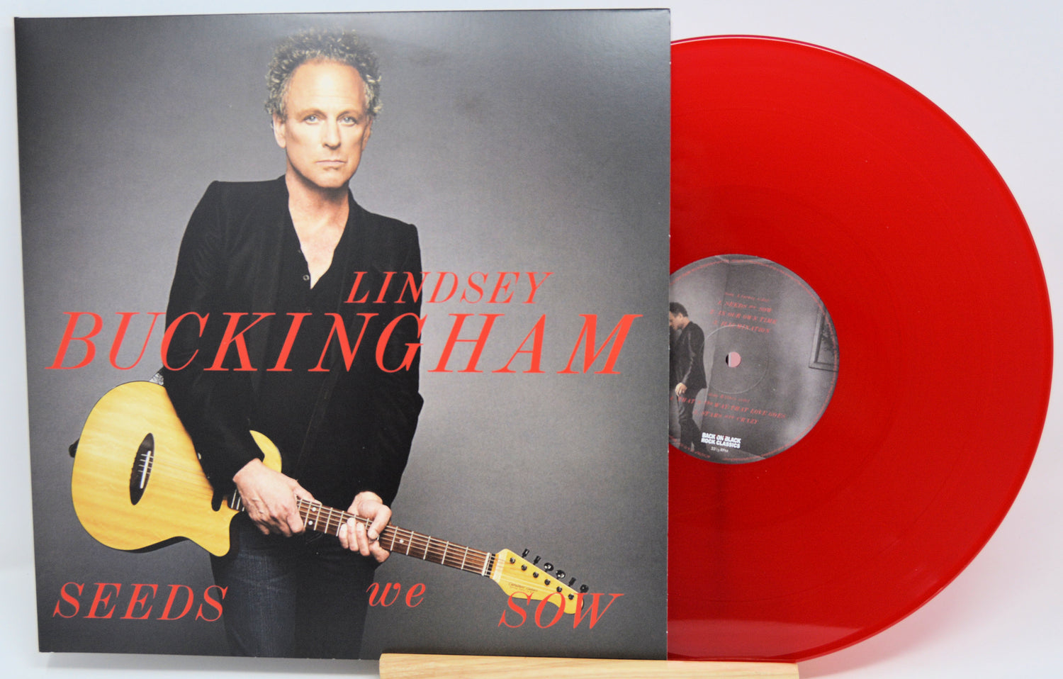 Lindsey Buckingham's 'Seeds We Sow' 12-inch vinyl record shown with its album cover and a translucent red vinyl disc on a white background.