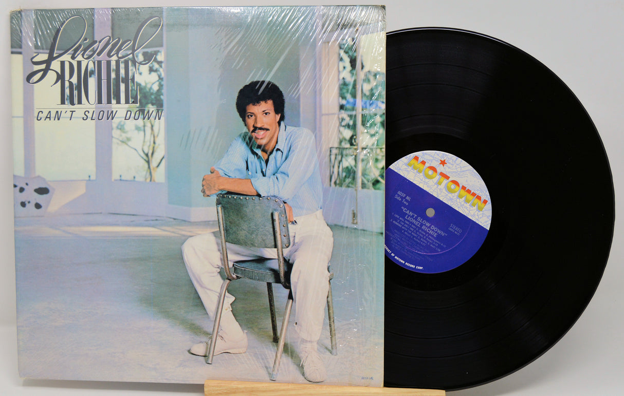 Vinyl record with cover featuring a person sitting on a chair, with 'Lionel Richie Can't Slow Down' album visible.