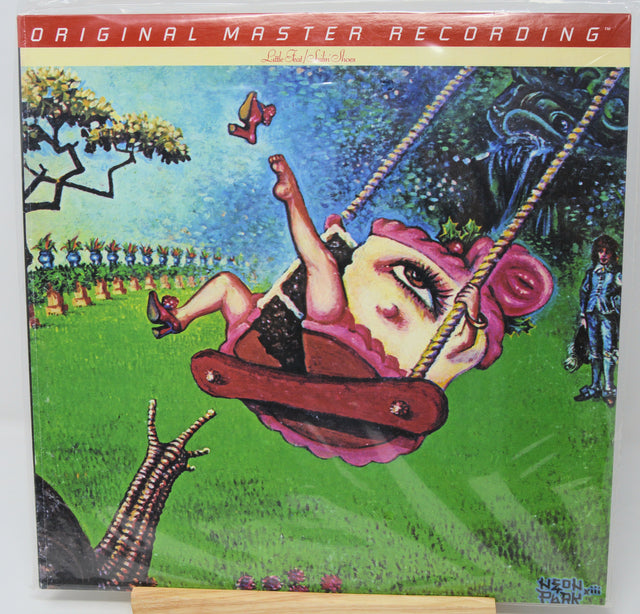The album cover of Neil Young's 'Harvest & Remembrance' on a vinyl record, featuring a surreal illustration of a woman on a swing in a grassy field under a blue sky.
