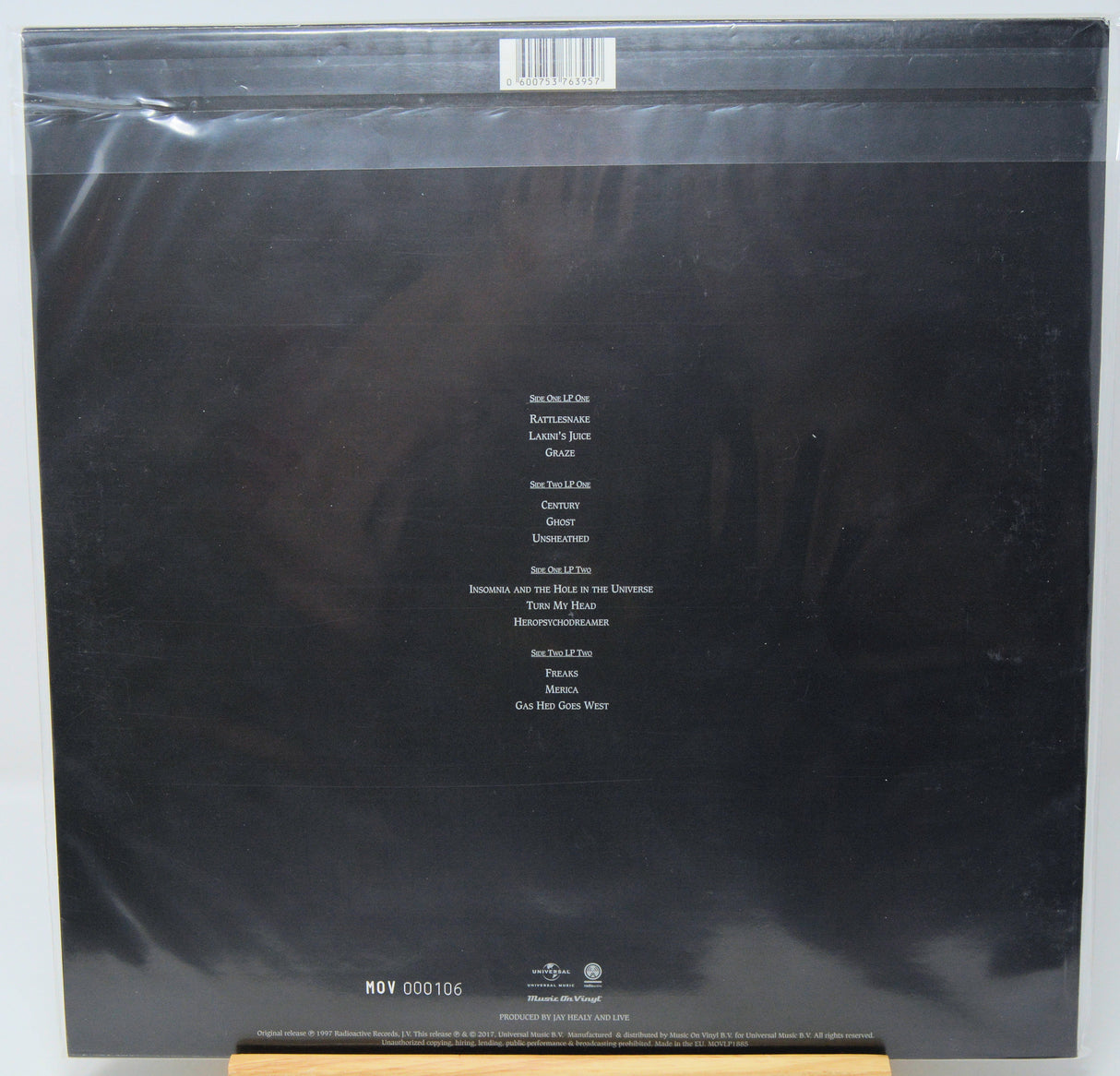 The back cover of a vinyl record in its original shrink wrap, featuring a black background with white track listing text and a barcode at the top.