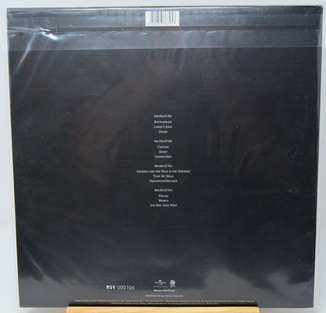 The back cover of a vinyl record in its original shrink wrap, featuring a black background with white track listing text and a barcode at the top.