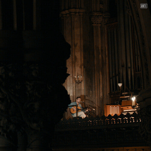 Musician playing guitar on stage beside a pipe organ in a dimly lit cathedral
