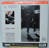 Back cover of a vinyl record sleeve for 'One Time One Night' by Bushbaby & Los Logos, featuring a large black-and-white photo of two children in a dark room, track listing text, and orange accents on a white background.