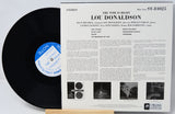 A vinyl record partially pulled from its printed album sleeve, showing the black disc with a blue-and-white label beside the white cover art for Lou Donaldson's 'The Time Is Right'.