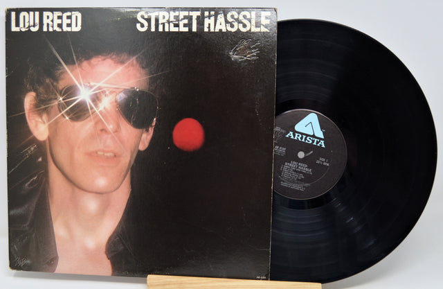 Vinyl record with cover featuring a person wearing sunglasses and a red dot, on a white background.