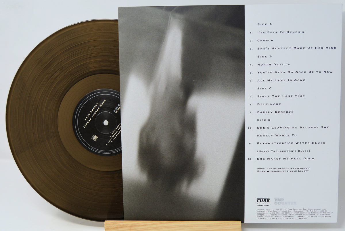 A vinyl record partially pulled from its sleeve, displayed on a small wooden stand against a white background. The record is translucent gold, and the sleeve features a black-and-white abstract photo on the front and a tracklist on the back.