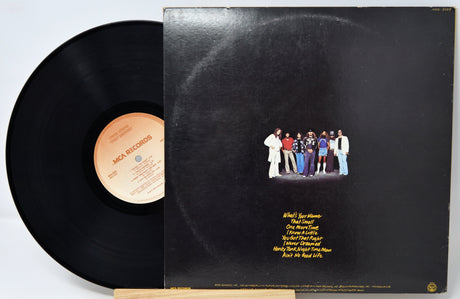 A black vinyl record partially pulled from its sleeve, showing the back cover artwork. The record label reads 'Mick McCallister' and the sleeve features a small group photo with yellow tracklist text on a black background.