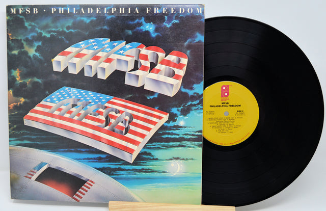 Vinyl record with cover featuring abstract designs and American flag, on a light gray background