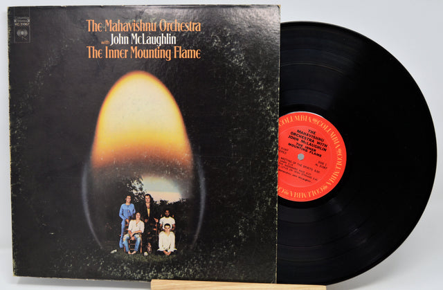 Vinyl record album for 'The Inner Mounting Flame' by The Mahavishith Orchestra and John McLaughlin, showing the black cover with an orange-yellow oval graphic and the black record partially pulled out, revealing a red-orange center label.