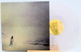 Album cover with a person standing on a beach and a yellow disc object.