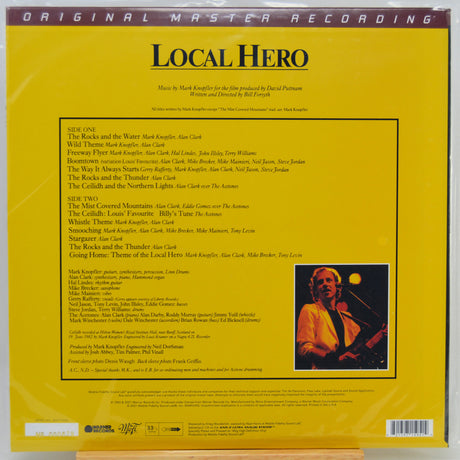 The back cover of the Local Hero vinyl record album, showing a bright yellow background with black text listing track titles, credits, and a small color photograph of Mark Knopfler on the right.
