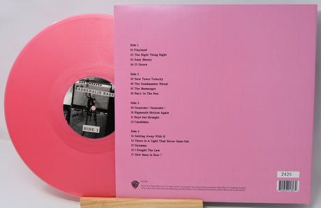 Pink vinyl record with sleeve showing tracklist on a light gray background