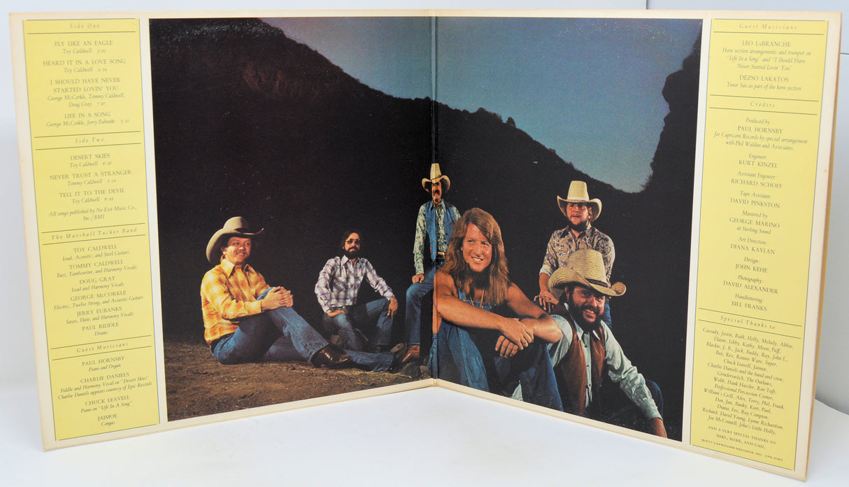 Album cover with a group of people in cowboy hats sitting on a mountain, flanked by yellow text pages.