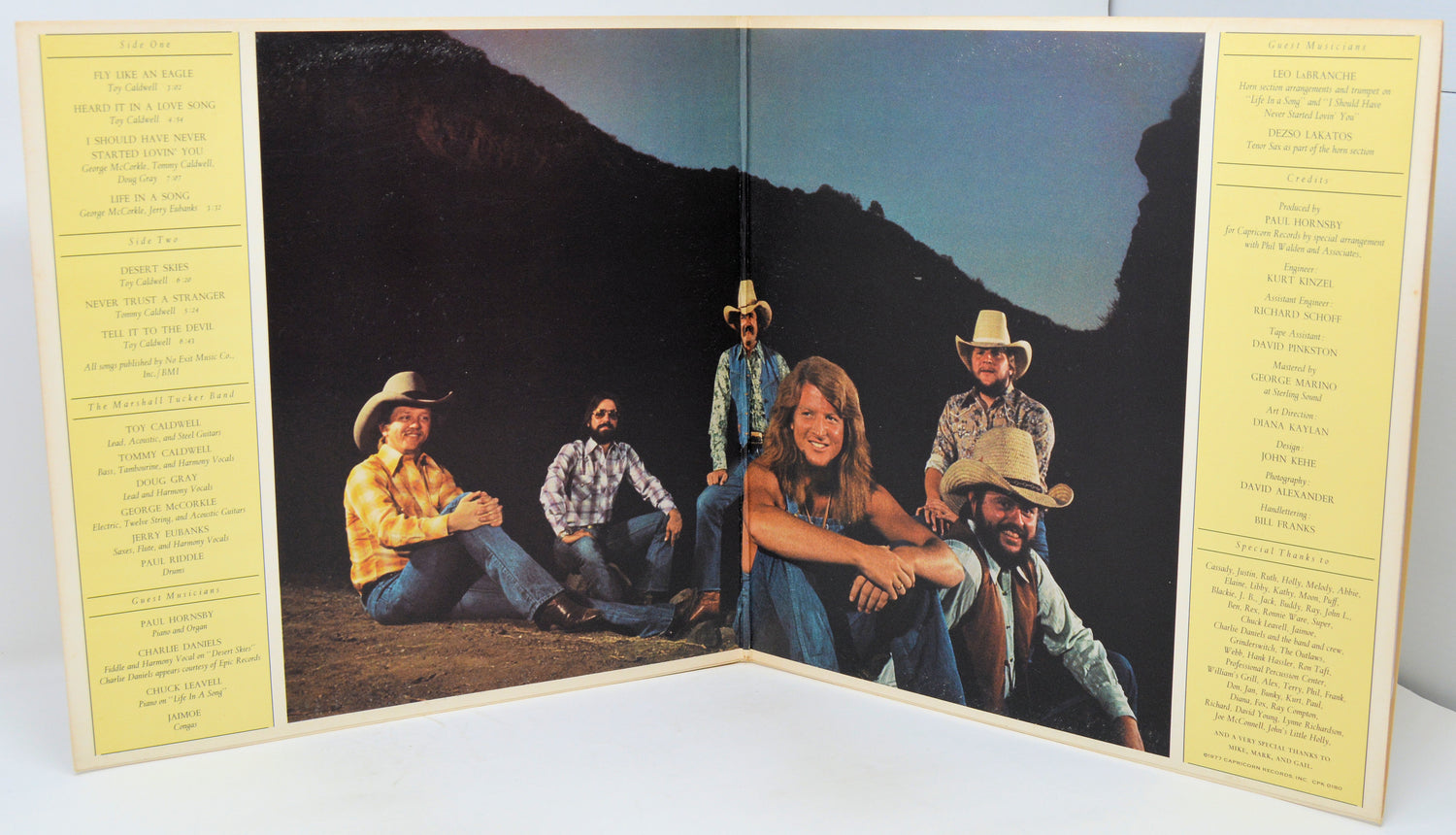 Album cover with a group of people in cowboy hats sitting on a mountain, flanked by yellow text pages.