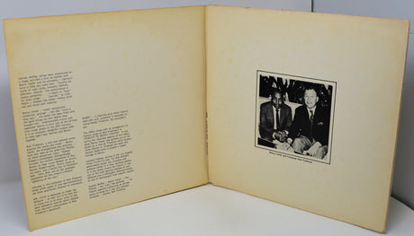 Open book with text on one page and a black and white photo of two men on the other, against a gray background.