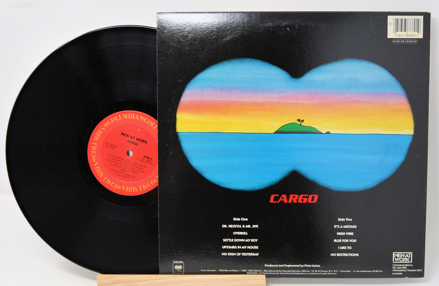Vinyl album by Men At Work title Cargo showing the record and back cover which includes a drawing of an island view through binoculars and a song title listing in text.