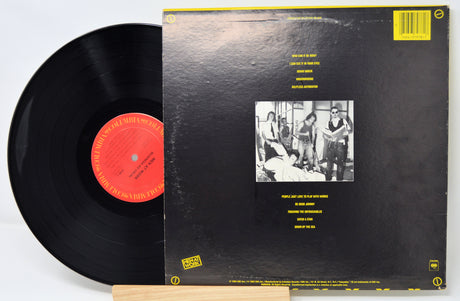 Vinyl record with black cover featuring a group photo and text on a white background
