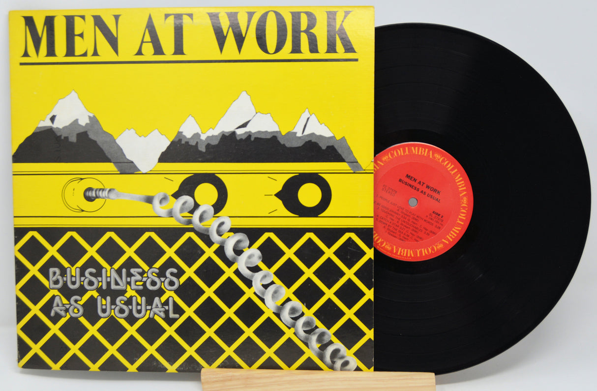 Vinyl record with 'Men at Work' album cover featuring a yellow background with mountain graphic and text.