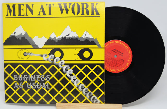 Vinyl record with 'Men at Work' album cover featuring a yellow background with mountain graphic and text.