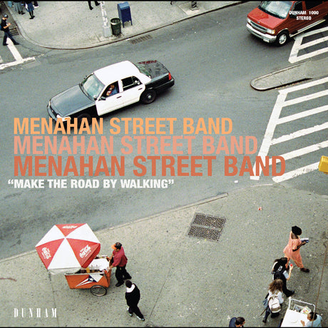 The image depicts a vinyl record cover for 'Make The Road' by Menahan Street Band. It shows a bustling city street scene with pedestrians, a car, a truck, and a red umbrella, complementing the album's urban-soul vibe.