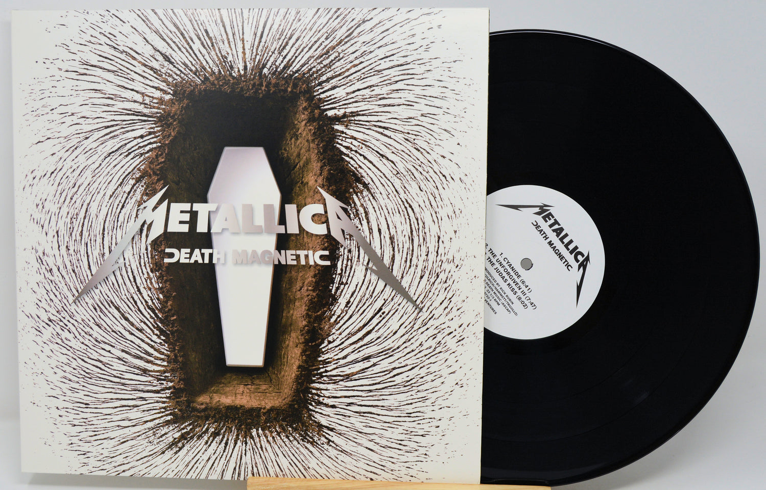 Metallica's 'Death Magnetic' vinyl record shown with its illustrated album cover sleeve and the black LP partially pulled out, on a light gray background.