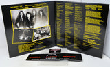 Metallica 'Heavier Than Never' CD album package shown open to the back insert, with printed black-and-white band photos, tracklist text in yellow, and a small printed card in front on a white background.