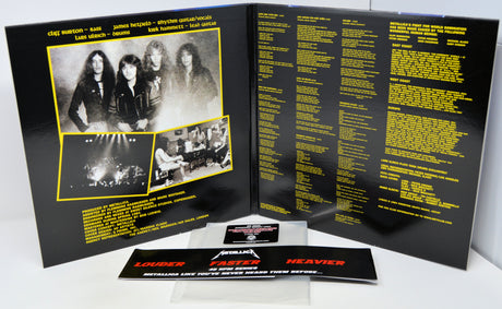 Metallica 'Heavier Than Never' CD album package shown open to the back insert, with printed black-and-white band photos, tracklist text in yellow, and a small printed card in front on a white background.