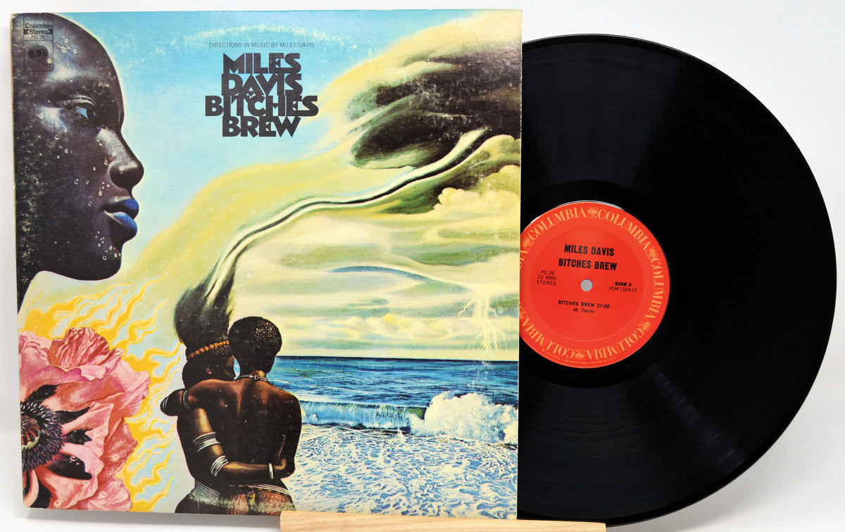 Miles Davis 'Bitches Brew' vinyl record shown with the illustrated album cover on the left and the black LP record partially visible on the right against a white background.