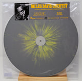 A Miles Davis Quintet vinyl record package in a clear plastic sleeve, displayed on a small wooden stand. The record is dark gray with a bright yellow burst pattern radiating from the center, and the sleeve features a black-and-yellow album cover label.