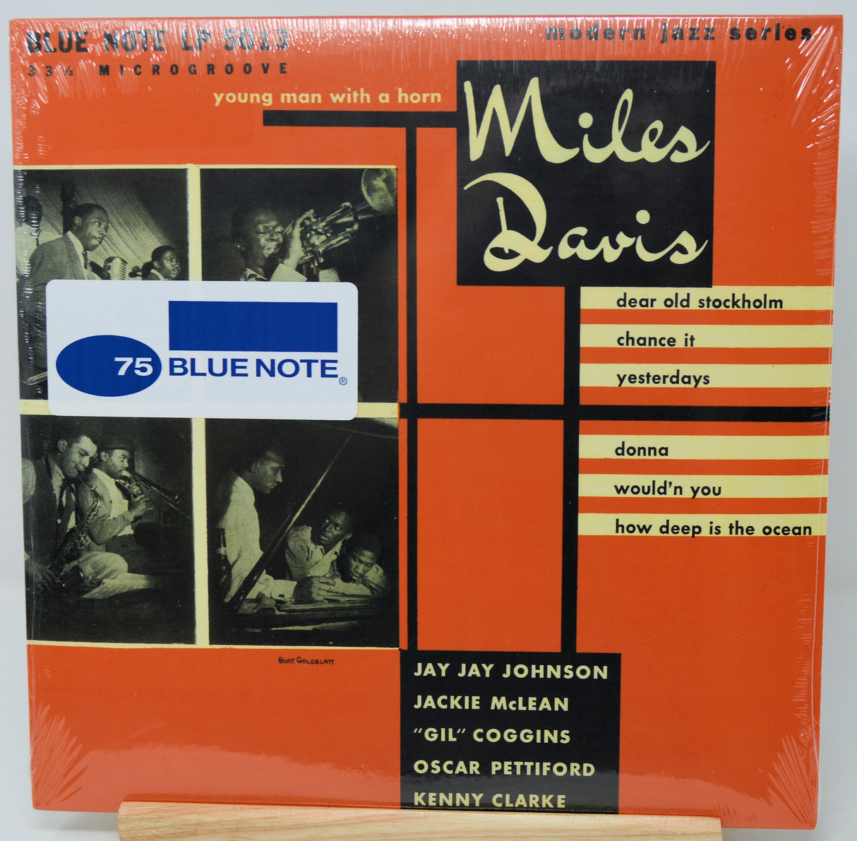 Miles Davis '75 Blue Note' vinyl record album cover, sealed in plastic shrink wrap, displayed on a wooden stand against a white background.