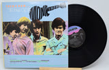 Vinyl record with cover featuring a band on a light gray background