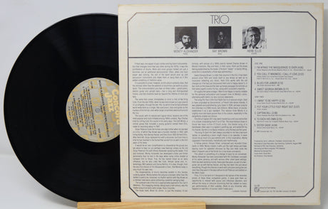 A vintage vinyl record partially pulled from its printed outer sleeve, showing the black record with a gold label on the left and the cream-colored back cover with text and small portraits on the right.